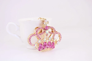 Dettaglio portachiavi a corona dorata con strass rosa appoggiato a una tazza bianca