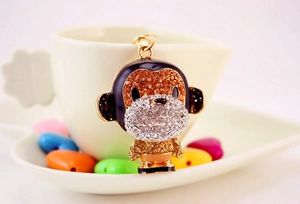 Close-up of alloy monkey keychain with orange rhinestones and enamel on a white mug
