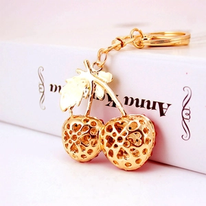 Charming hollowed-out golden cherry keychain with red beads and elegant leaf detail