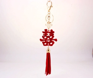 Close-up of golden wedding keychain featuring red crystals Double Happiness and silk tassel