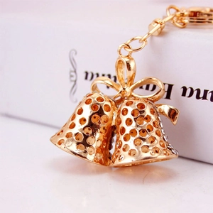 Golden double bell keychain with bow design and white rhinestones on white book background