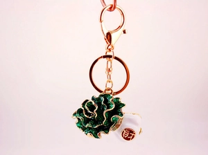 Close-up of green cabbage keychain with gold edges and red Cai lucky charm