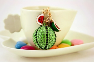 Charming rhinestone watermelon keychain pendant hanging on a cozy ceramic coffee cup edge