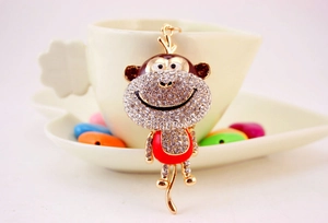 Detail of golden alloy monkey keychain with white rhinestones and red enamel coating