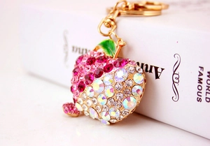 Close-up of pink and AB crystal rhinestone apple keychain with gold clasp on a book