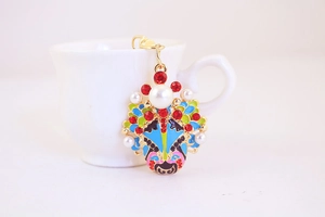 Close-up of a Peking Opera mask keychain with gold alloy, colorful oil drip, and red crystals