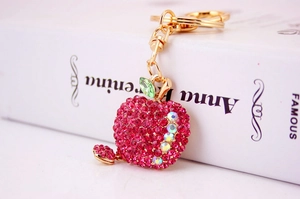 Detail of pink rhinestone apple keychain with heart pendant on a white book base