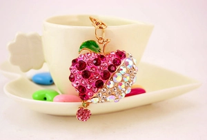 Detailed macro of pink rhinestone apple keychain with gold clasp on a white coffee cup