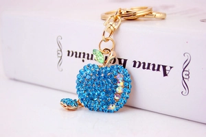 Detail of sapphire blue rhinestone apple keychain with gold clasp on a book