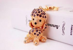 Close-up of golden poodle keychain with purple rhinestones on a white book prop