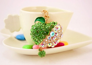 Close-up of apple keychain with green rhinestones hanging on a white coffee cup