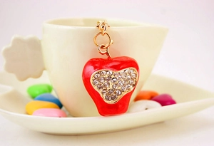 Detail of red apple pendant with sparkling rhinestones on a white coffee cup