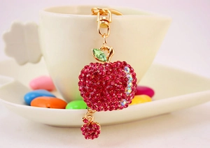 Detailed view of red rhinestone apple keychain with gold clasp on white coffee cup background
