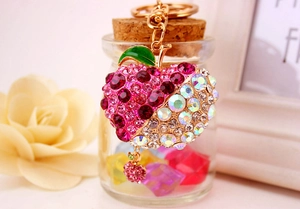 Detail of rose pink apple keychain with AB crystals and golden ring on glass bottle background