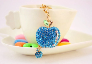 Macro view of blue rhinestone apple keychain with gold finish and green leaf detail