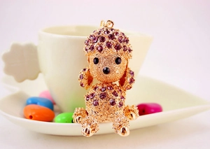 Detail view of gold poodle keychain with sparkling purple rhinestones near a coffee cup