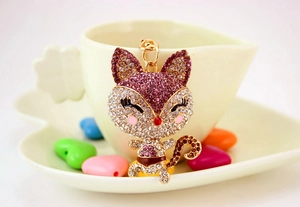 Close-up of cute cartoon fox keychain with pink and purple rhinestones on a ceramic cup