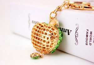 Close-up of golden apple keychain with green rhinestones and hollow heart mesh detail