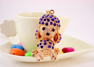 Detail of blue rhinestone poodle keychain on a white ceramic tray with colorful beads
