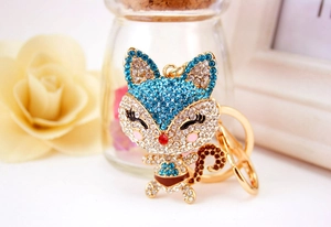 Close-up of golden cartoon fox keychain with blue rhinestones and cream roses