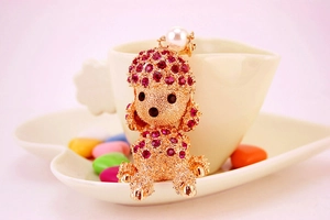 Detail of pink rhinestone poodle keychain leaning against a white cup with a pearl accent