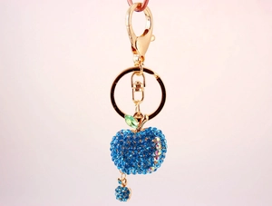 Close-up of golden apple keychain with sparkling blue rhinestones and green leaf detail