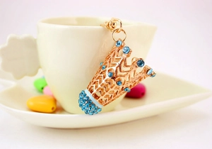 Détail d'un porte-clés badminton en or rose orné de strass bleu clair sur une tasse à café