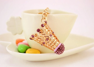 Détail d'un porte-clés badminton doré avec strass violets posé sur une tasse de café