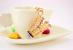 Détail d'un porte-clés badminton doré avec strass blancs posé sur une tasse à café en céramique
