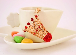 Détail d'un porte-clés couronne dorée avec strass rouges sur le rebord d'une tasse