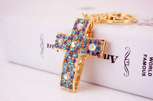 Gros plan sur un porte-clés croix dorée orné de strass bleus et cristaux étincelants