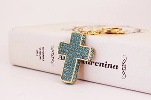 Nahaufnahme von goldenem Kreuz-Schlüsselanhänger mit blauen Kristallen auf Buch
