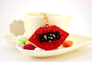 Detailed view of red rhinestone kiss lip keychain with gold clasp on a ceramic cup