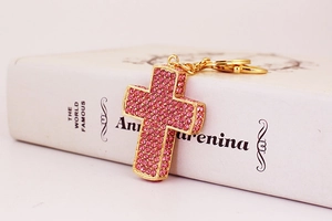 Makro-Detail des goldenen Kreuz-Schlüsselanhängers mit rosa Kristallen auf Buch
