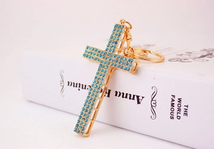 Detail shot of the golden cross keychain featuring vibrant light blue rhinestones on a book