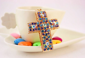 Détail du pendentif croix en métal doré avec strass colorés sur une surface blanche