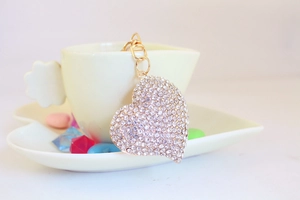 Detailed view of a sparkling heart keychain with white rhinestones on a ceramic cup edge