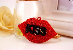 Detail of red rhinestone lips keychain with KISS text and polished gold ring