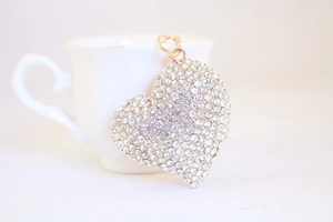 Macro shot of sparkling rhinestone heart pendant hanging on a white ceramic mug edge