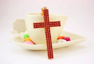 Close-up of golden cross keychain with red rhinestones on a coffee cup saucer