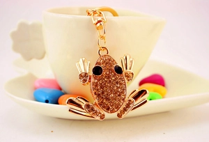 Detailed close-up of a golden frog keychain with champagne rhinestones on a coffee cup