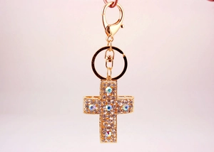 Détail d'un porte-clés croix dorée serti de cristaux blancs et AB avec fermoir mousqueton