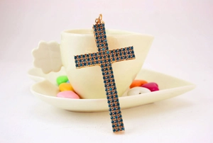 Detail shot of a golden cross keychain featuring blue rhinestones on a ceramic cup