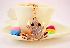 Detail of a sparkling golden frog keychain with white crystals on a white coffee cup
