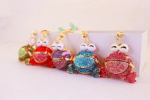 Détail de cinq porte-clés grenouille en strass colorés avec anneaux en métal doré