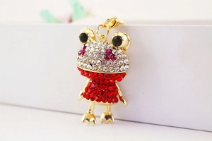Nahaufnahme eines glitzernden Frosch-Schlüsselanhängers mit rotem Kleid und Goldring