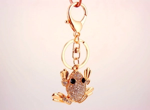 Detailed close-up of a gold frog keychain charm with white crystals and black gem eyes