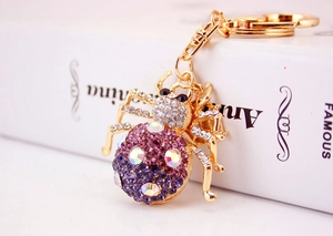 Macro view of a gold-plated spider keychain with purple and pink gradient rhinestones