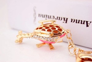 Close-up of golden helicopter keychain with pink enamel details and sparkling rhinestones