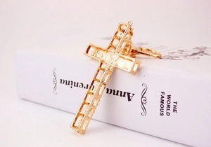 Close-up of golden hollow cross keychain pendant leaning on a white book edge
